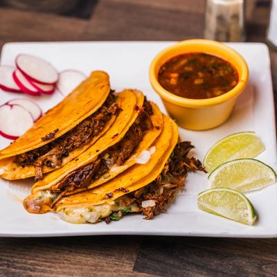 Birria tacos with, lime wedges, radish slices, and birria sauce on the plate.