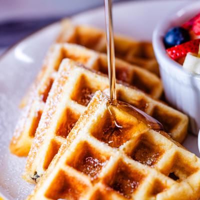 Syrup drizzling over waffles beside a cup of fruit.