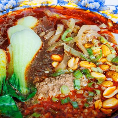 Close-up of spicy noodle soup with bok choy, peanuts, and chili oil.