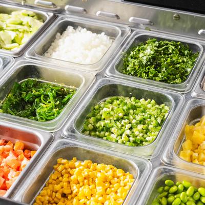 Assorted chopped vegetables in a salad bar setup.