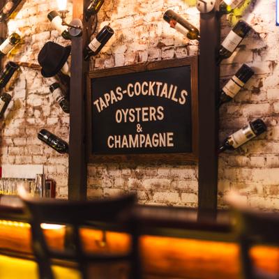 Wine rack with a sign offering tapas, cocktails, oysters and champagne.