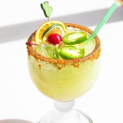 Jalapeno margarita in a chili-rimmed glass with citrus and cherry garnish.