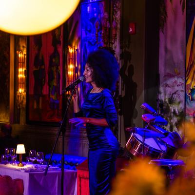 Singer holding the microphone during live entertainment, colorful artwork in the background.