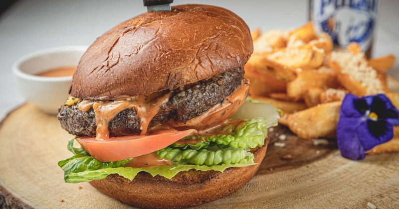 Burger with lettuce, tomato, pickles and cheddar, a side of fries and sauce