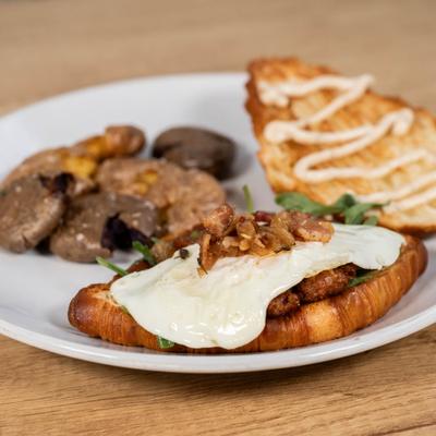 A savory breakfast croissant sandwich served with a side of crispy potatoes.
