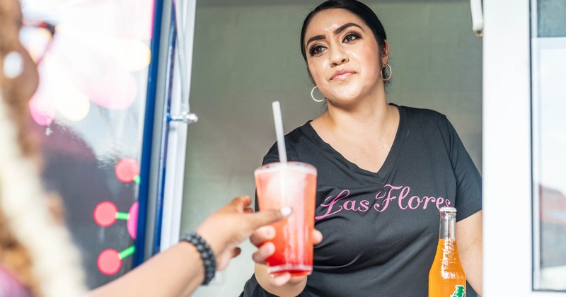 An employee serves customer a drink at the food truck window