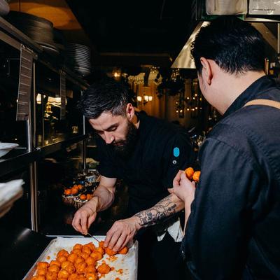 Two chefs preparing orange dough balls for baking.