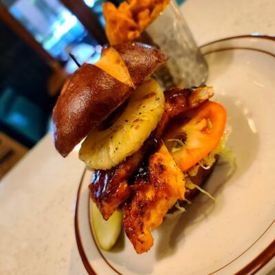 A BBQ salmon sandwich with grilled pineapple on a pretzel bun served with your choice of side..
