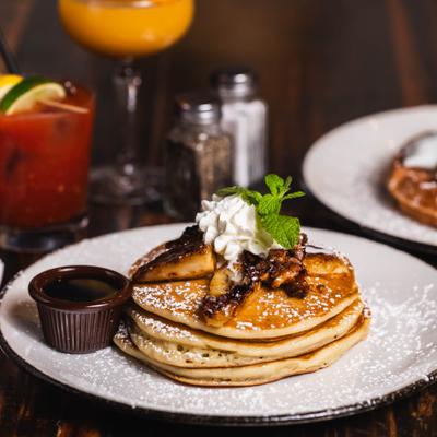 A stack of pancakes topped with bananas, whipped cream, and mint next to syrup.