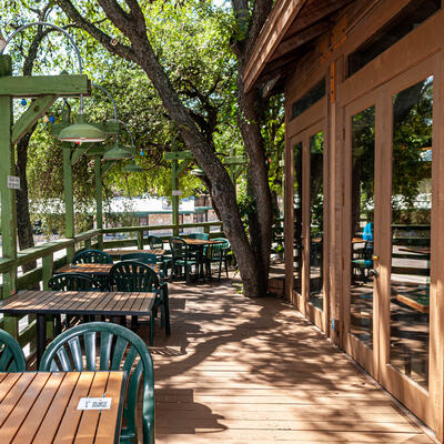 Wooden patio with green chairs and tables on tree-shaded deck.