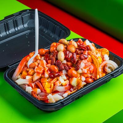 Tortilla chips topped with various ingredients such as peanuts, corn nuts, and a red sauce.