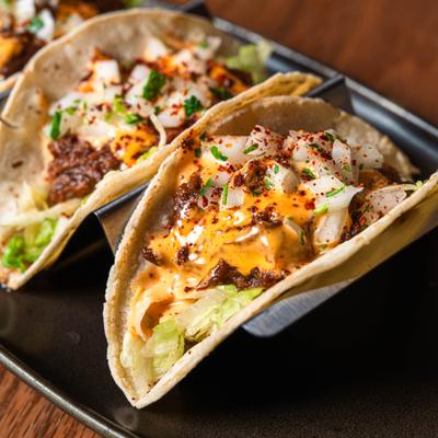 Tacos topped with seasoned meat, shredded lettuce, onions, orange sauce, and chili flakes..