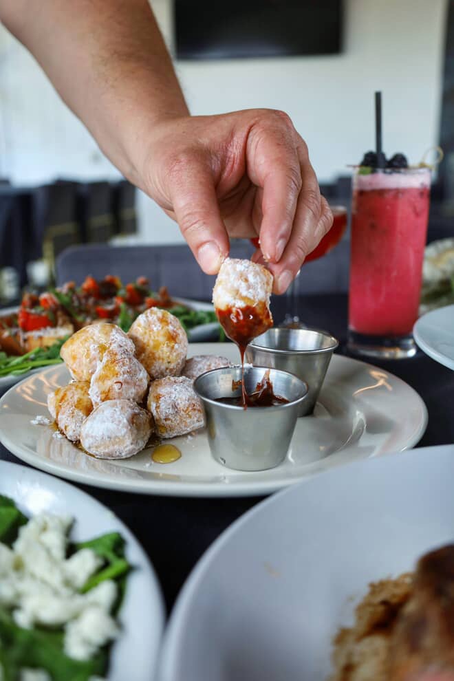 Hand dipping powdered pastry into a cup of chocolate sauce