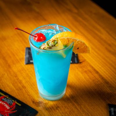 A glass of Blue Hawaiian, garnished with a cherry, a pineapple wedge, and a lemon slice.