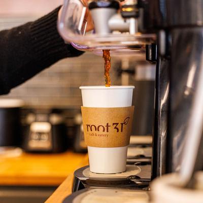 A barista pouring coffee into a paper cup from a machine.