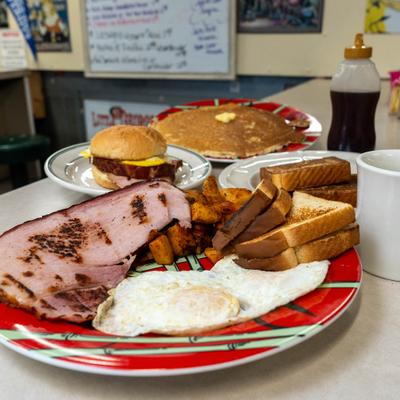 Ham steak served with eggs, home fries and toast, alongside other meals.
