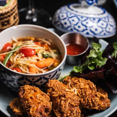 Crispy fried chicken served with a papaya salad, greens, and a side of dipping sauce.