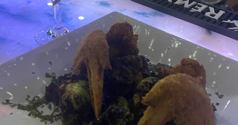 A plate of fried chicken wings served on a bed of roasted Brussels sprouts