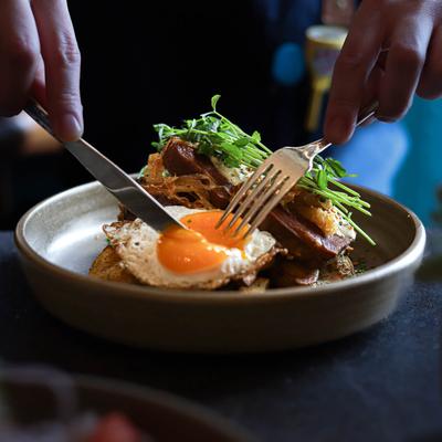 A person cutting through a fried egg with a knife and fork.