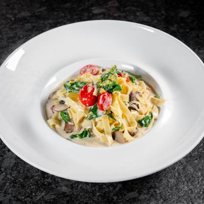 Tagliatelle with cherry tomatoes, spinach, and mushrooms in a creamy sauce.