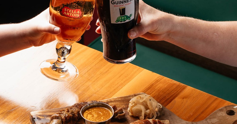 Two hands clinking beer glasses over a wurst board