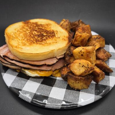 A grilled ham and cheese sandwich with seasoned, golden brown potato cubes.