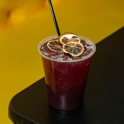 A refreshing dark colored drink served in a plastic cup with dry citrus wheels.