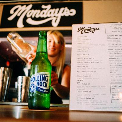 Bottle of beer and a menu displayed on the counter with bartender in the background.