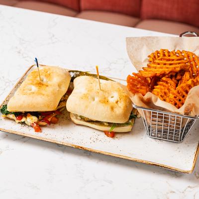 A sandwich on ciabatta bread, cut into two halves, and a side of waffle fries.