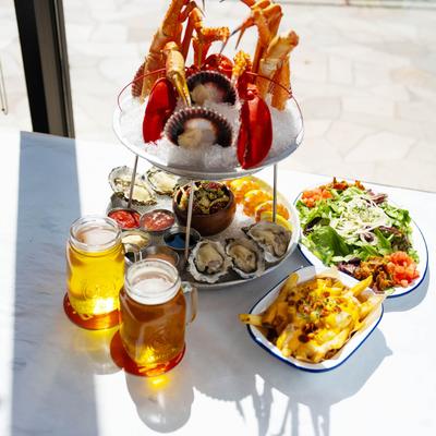 Seafood tower, sweet onion salad, chowder fries, and two glasses of beer on a table.