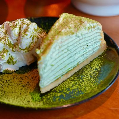 Slice of a Matcha cake, served with whipped cream and dusted with matcha powder.