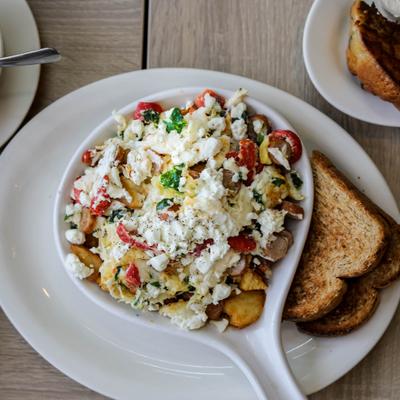 Breakfast skillet with scrambled eggs, potatoes, vegetables, cheese, and toast.