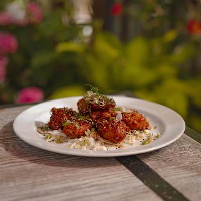 Fried chicken bites served on a white plate over slaw, garnished with herbs.