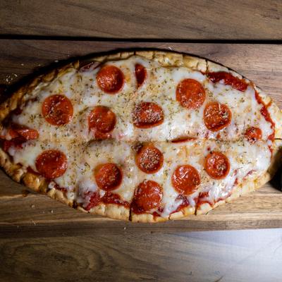 Flatbread topped with melted mozzarella cheese and pepperoni, served on a wooden board.