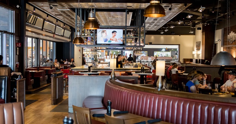 Interior of a spacious restaurant with curved red booths, wooden tables, pendant lights