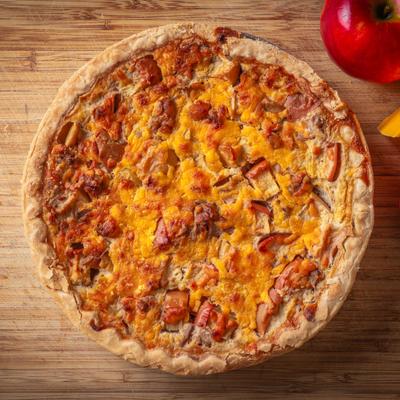 Apple cheddar quiche on a wooden table with fresh red apples, overhead view.