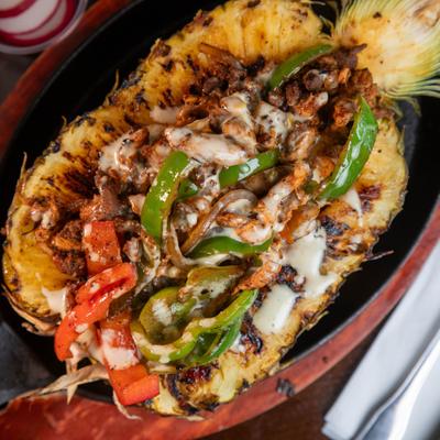 Pineapple fajitas featuring a grilled pineapple half filled with meats, veggies and cheese.