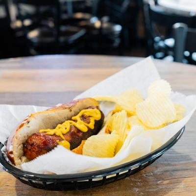 Hot dog topped with mustard, served with chips.