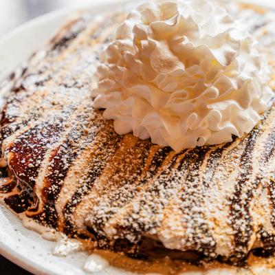 Chocolate crepe topped with whipped cream and powdered sugar drizzle.