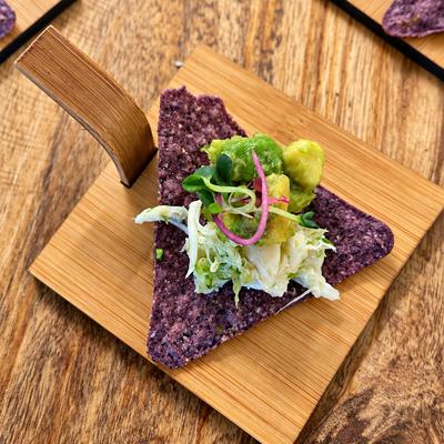 Purple corn tortilla chip topped with guacamole, shredded cabbage and microgreens.