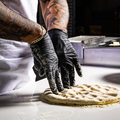 Hands in black gloves stretching pizza dough.