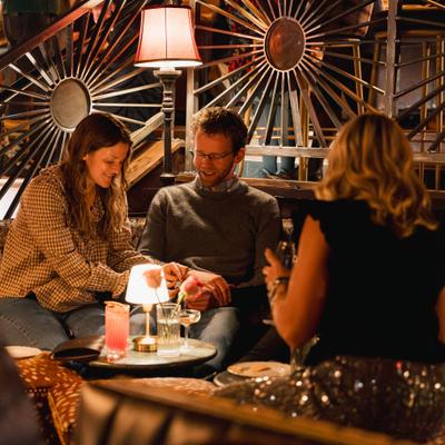 Three people sit together in a cozy bar with warm lighting.