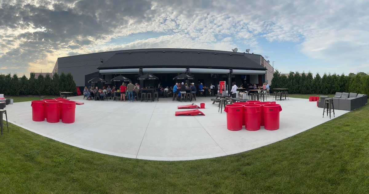 A spacious patio with guests, oversized games, and parasols under a cloudy sky