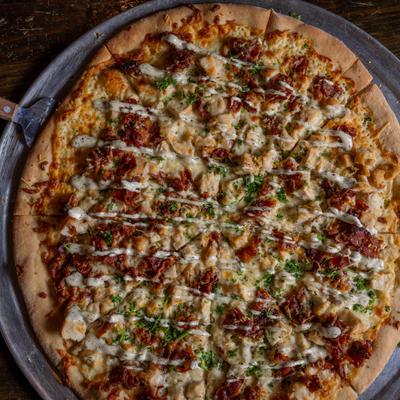 Pizza topped with chicken, crispy bacon, and sauce drizzle.
