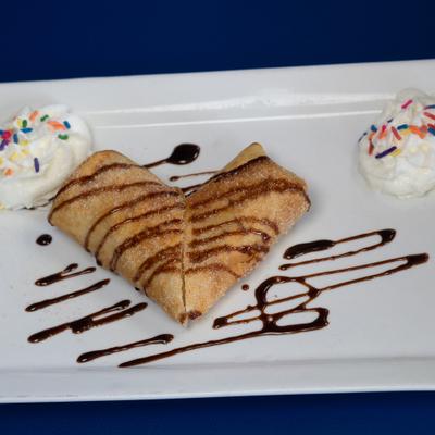 Mexican fried cheesecake chimichanga with whipped cream, sprinkles, and chocolate drizzle.