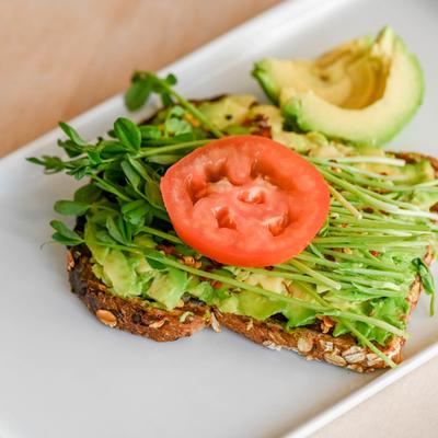 Avocado toast, with pea shoots, red pepper flakes, and tomato.