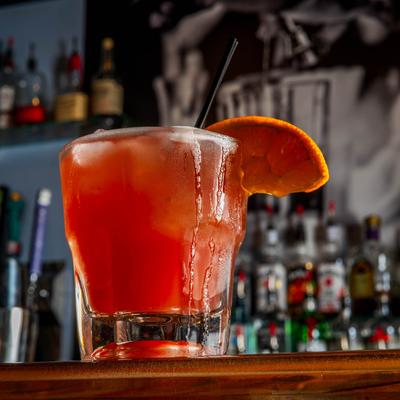 A glass of red craft cocktail sitting on bar counter.