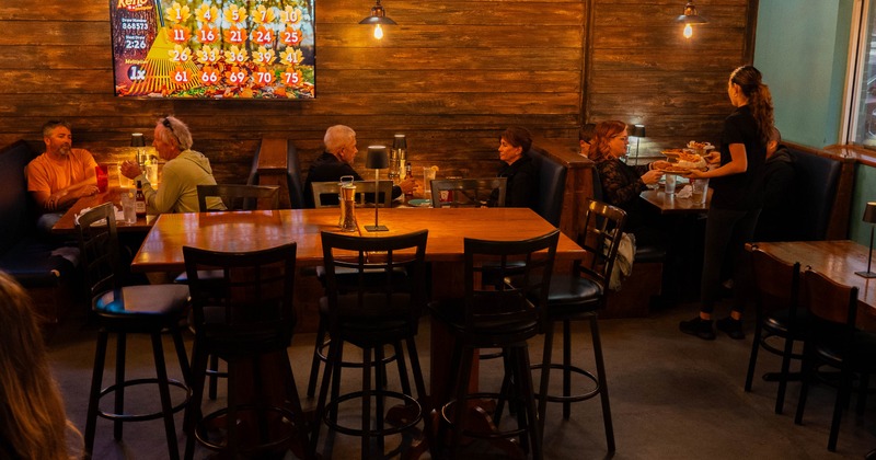 A dimly lit restaurant interior with  tables and a large TV screen