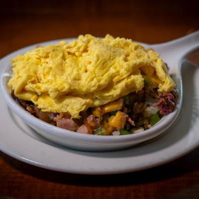 Scrambled eggs served over hearty hash mix in bowl.