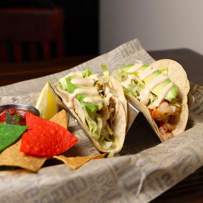 Two grilled fish tacos with corn chips.